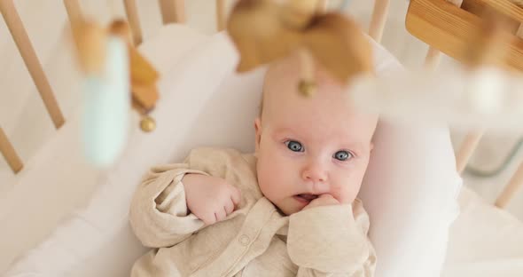 A Cute Little Baby Lying in a Baby Crib on a White Blanket Wearing White Clothes Looking with