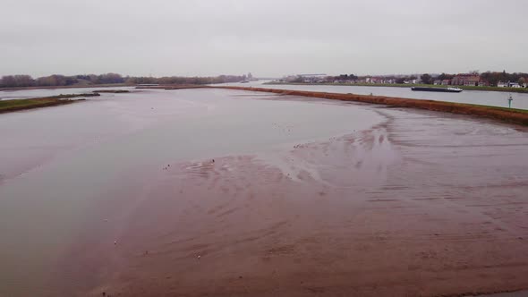 Aerial Rising Flying Over Flood Plain Beside Noord In Ridderkerk With Ship Passing By In Distance