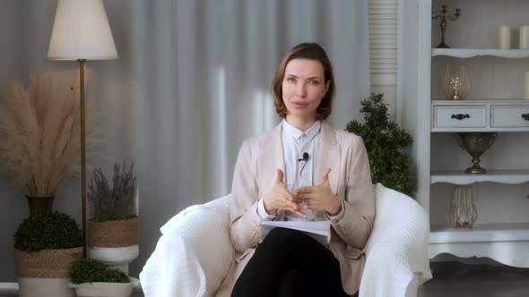 Smiling young woman, blogger, vlogger, influencer, sitting at home, talking, looking at the camera