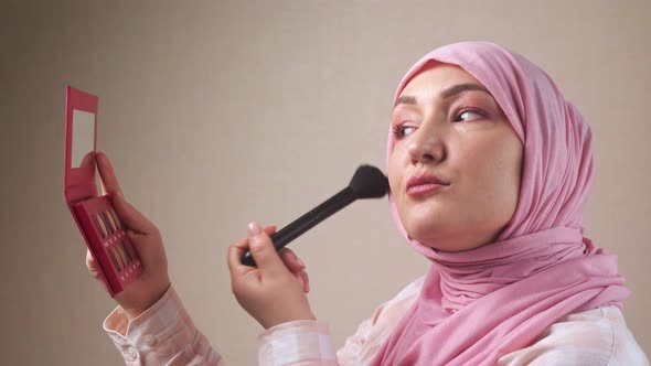 Woman in Hijab Applying Makeup with a Brush While Looking in the Mirror