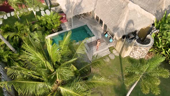Girl enjoying good weather in luxury villa hotel with private pool surrounded by palm trees.Aerial f