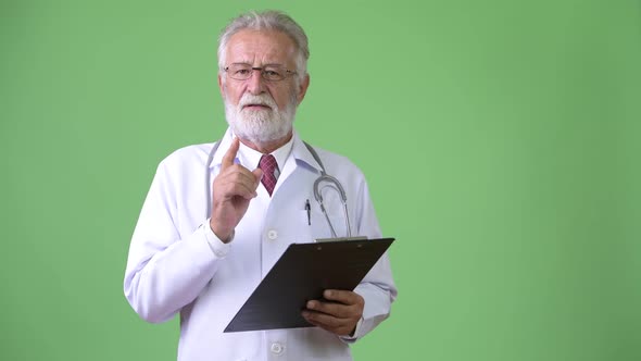 Handsome Senior Bearded Man Doctor Against Green Background