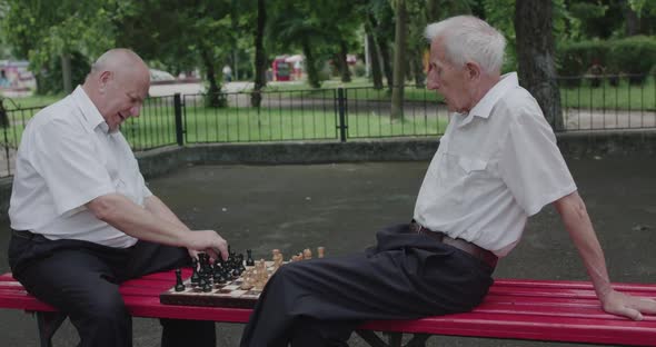 Two Seniors Friends in Suits Playing the Chess Game with Joy on a Street Bench