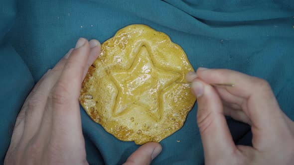 Man scratching dalgona candy made from sugar and soda with metal needle