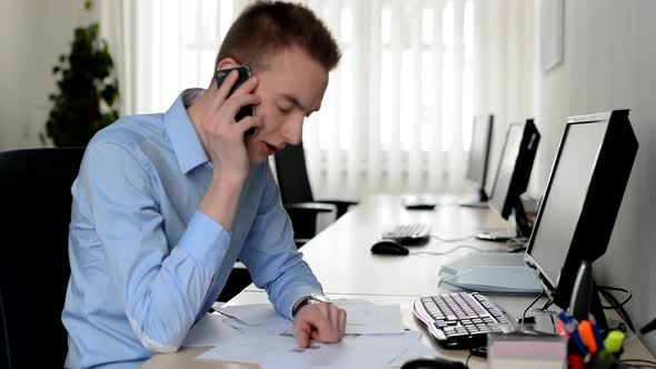 Young Handsome Man Works on Desktop Computer and Phone with Smartphone in the Office