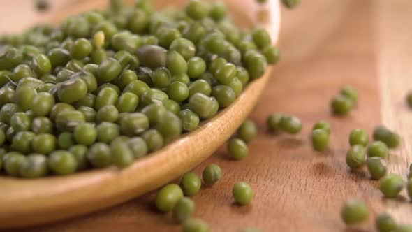 Green raw mung beans fall on a wooden spoon in a heap on a natural wood surface
