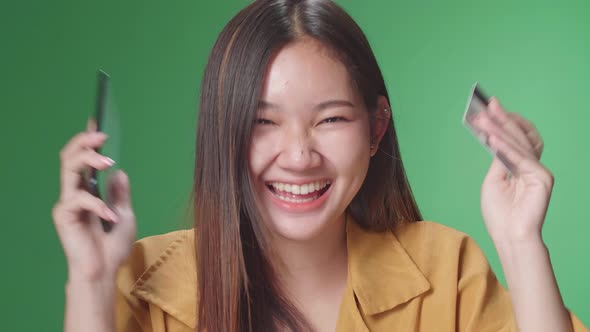 Asian Woman Using Mobile Phone With Credit Card And Celebrating In The Green Screen Studio