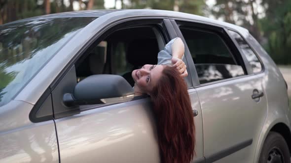 Zoom in to Happy Beautiful Woman with Long Red Hair on Driver's Seat Leaning Head on Car Door