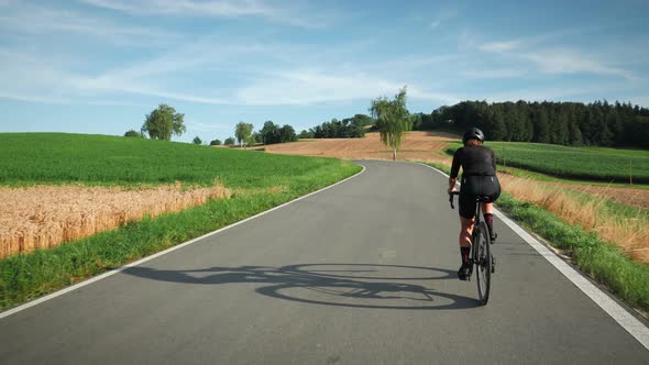 Female road cyclist riding on bicycle up an asphalt road in sunshine