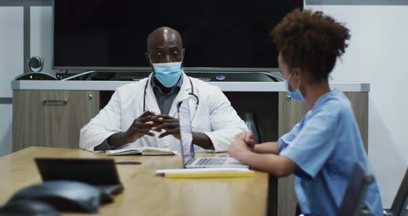 Diverse female and male doctors wearing face masks discussing in office
