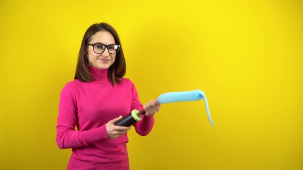 A Young Woman Inflates a Long Blue Balloon with a Pump on a Yellow Background. Girl in a Pink