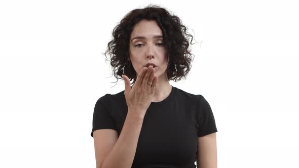 Attractive Young Woman with Short Curly Hair Wearing Casual Black Tshirt Blowing Air Kiss at Camera