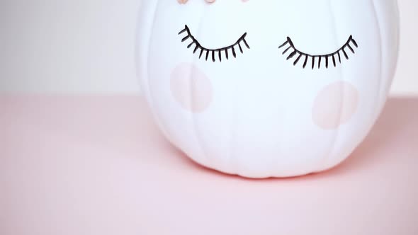 Craft pumpkin painted white and decorated with pink flowers as unicorn on pink background.