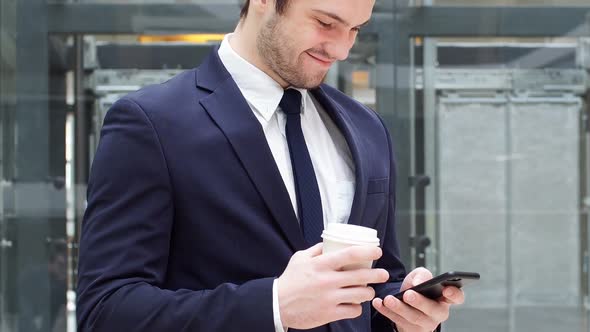 Young Confident Businessman Drinking Takeaway Coffee and Use Smartphone.