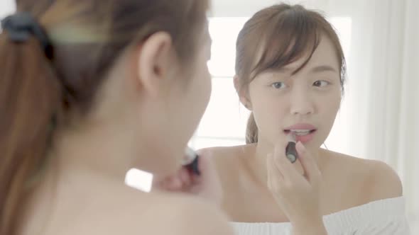 Beauty of young asian woman at the mirror applying and looking a makeup lipstick.