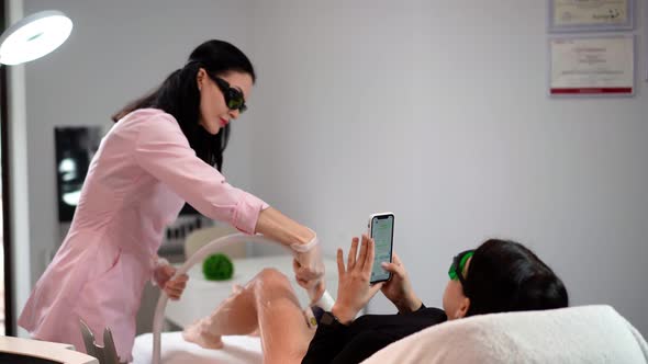Beautician Doing Laser Hair Removal on Slim Legs Woman in Beauty Salon. 