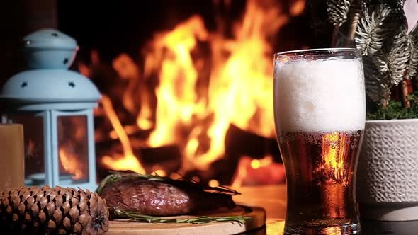Cold refreshing beer with foam in a glass with meat on a platter by fireplace