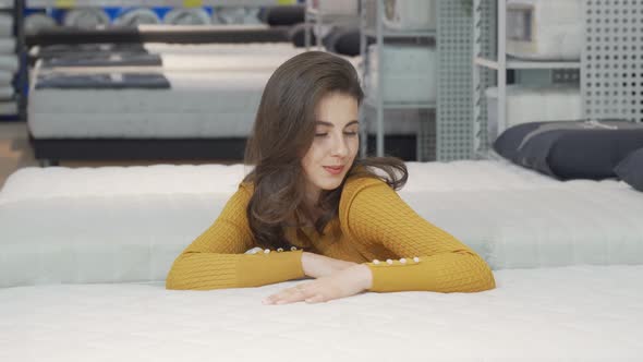 Beautiful Happy Woman Examining Orthopedic Mattress on Sale