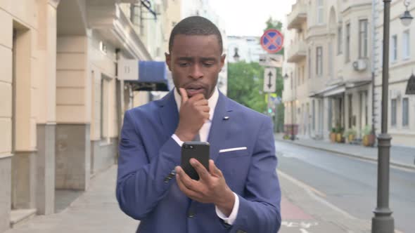 African Businessman Reacting to Loss on Smartphone While Walking on Street