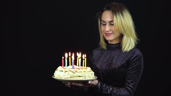 The Girl Holds a Holiday Cake with Candles. A Young Woman Is Standing in a Shiny Evening Dress