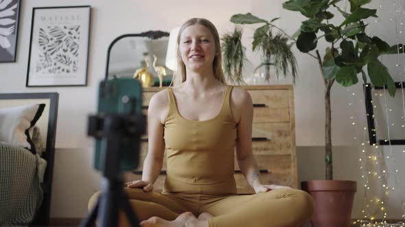 Woman Sits on Yoga Mat and Talks Using Phone on Tripod