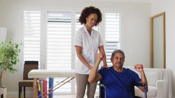 Mixed race female physiotherapist helping senior man exercise using dumbbells