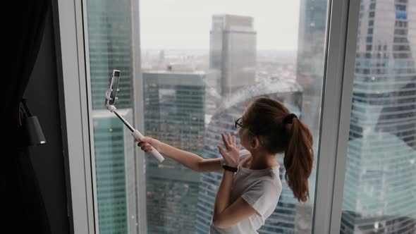 Modern Teenage Girl Taking a Selfie Near the Window in a Modern Apartment Overlooking the City From