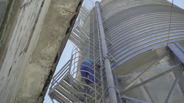 Wide Shot of Man in Uniform and Safety Helmet Walking on Enormous Cement Storage Silo. Huge