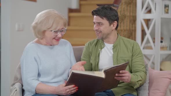 Medium Shot of Happy Cheerful Senior Woman and Adult Man Watching Photos in Album Laughing Recalling