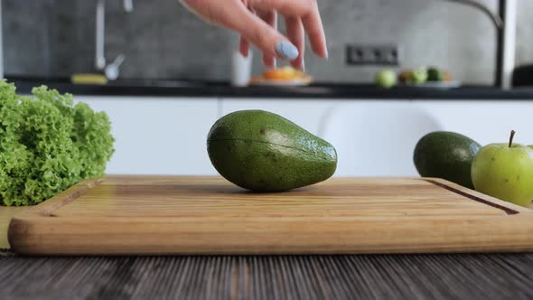 Women s Hands Hold Two Cut Halves of Fresh Green Avocado of the Kitchen Background