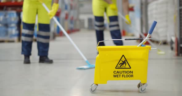 Cropped Shot of Worker Swearing Safety Overall Holding Mop Cleaning Floor in Warehouse