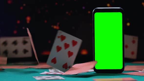 Smartphone With Green Screen Standing on Background of Falling Playing Cards