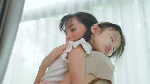 Asian beautiful loving mother holding sleeping napping baby girl in her arms with gently. alt