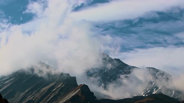 Timelapse Clouds Swirl Over a Mountain Valley a Snowy Peak in the Distance