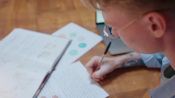 Young Man Studying at Home Writes in His Notes and Reads a Textbook