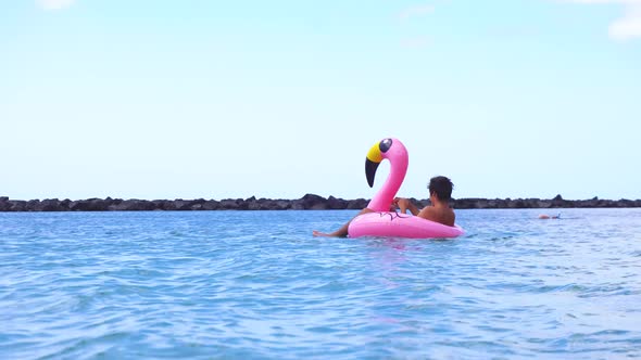 Young Male Swimming on Pink Inflatable Flamingo on Summer Sea