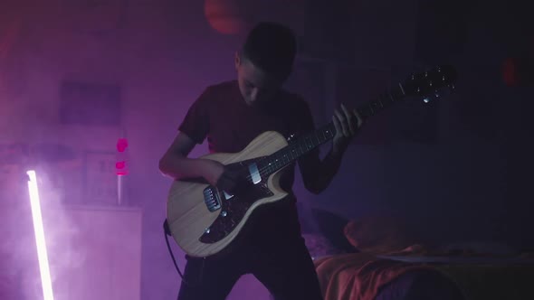 Teenager Playing Guitar Near Bed at Night
