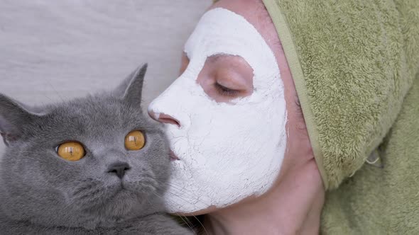 Woman in a Mask of White Clay on Face Holds a British Cat in Arms