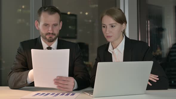 Business People Reading Documents in Office at Night 