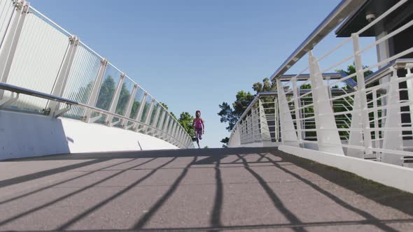 African american woman wearing face mask running on the city bridge