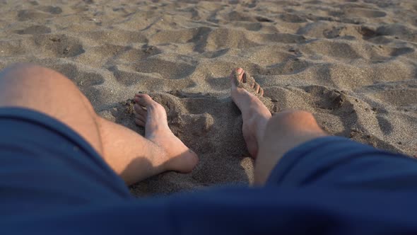 Male pushing sand with feet lying on sandy beach, low point-of-view of feet