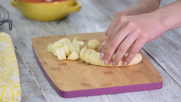 Close-up on woman cutting banana on cutting board.	
