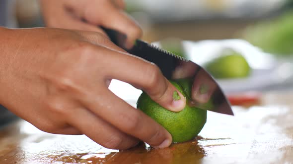 Close Up of Woman's Hands Slicing Green Lime on Wooden Cutting Board.