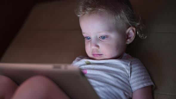 Child looking at a tablet sitting on a sofa. Little girl and internet