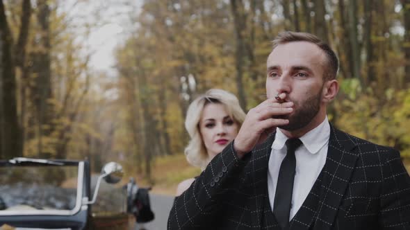 Lady Leans on Her Man Smokes Cigar and Looks in the Distance