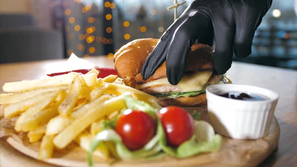 Closeup Hands of a Waiter is Cuts a Burger on a Wooden Round Tray