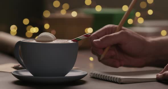 Slow Motion Man with Blue Cup on Wood Table in the Evening Making Shopping List for Holidays