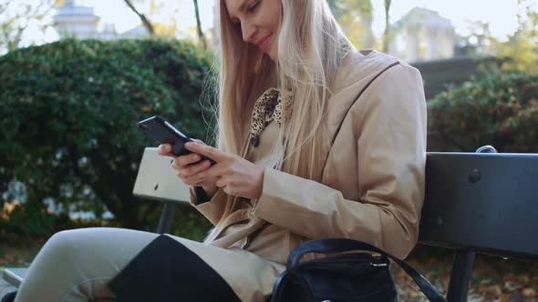 Pretty Girl in Stylish Jacket Using Smartphone in the Park at Sunny Day in Autumn Park.