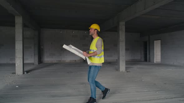 Wide image of caucasian engineer walking on construction site and browsing building plans.