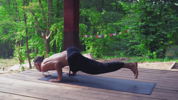 Man Performs Yoga Exercises Lifting One Leg and Bending the Other